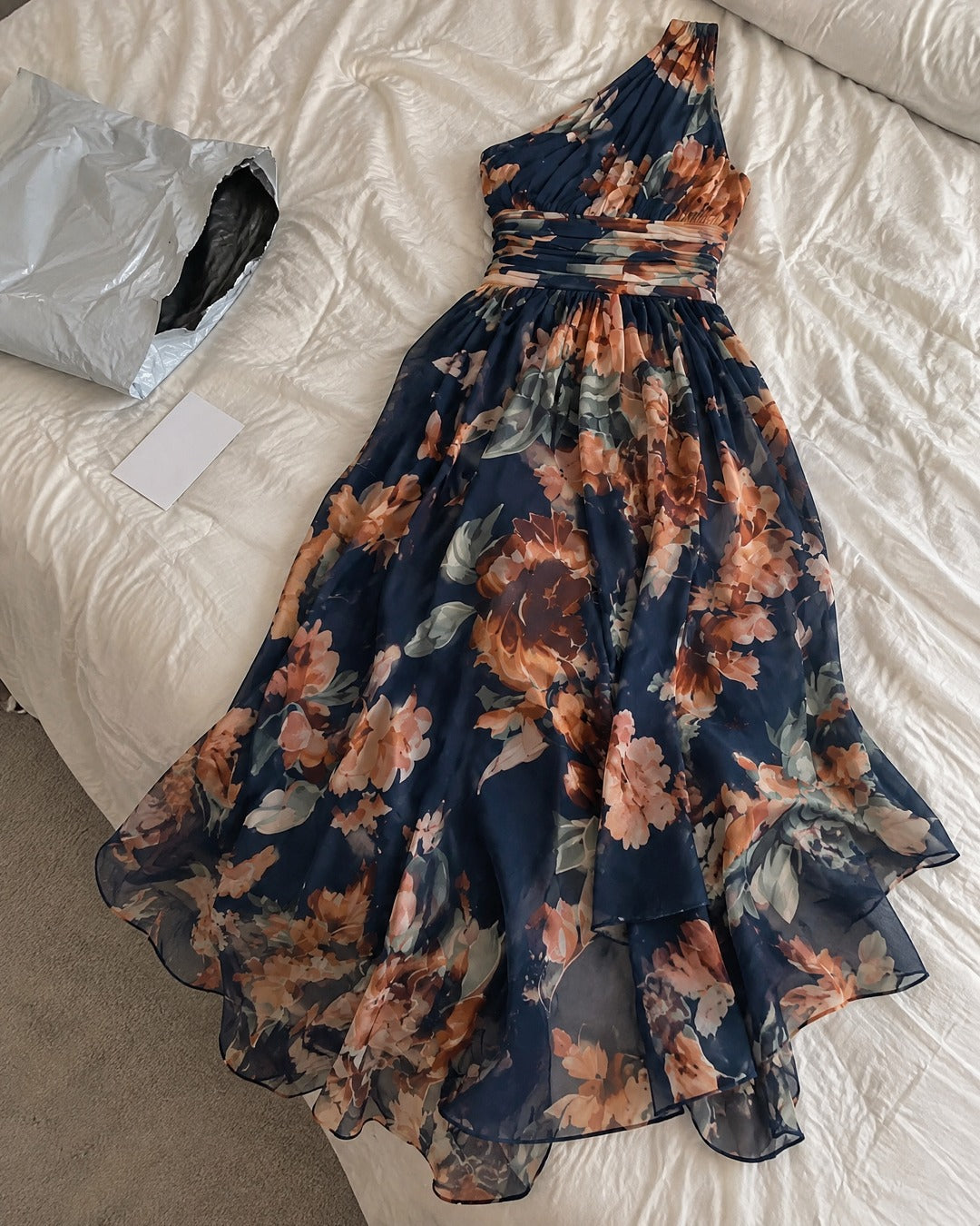 Celeste navy floral one-shoulder maxi dress laid flat on a bedroom bed
