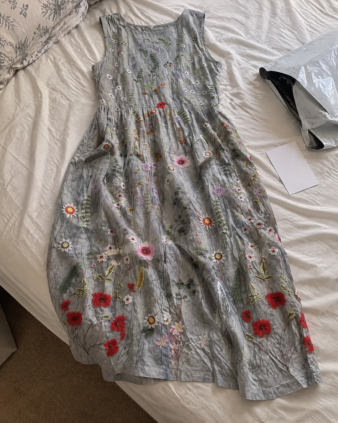 Agnes Wildflower grey sleeveless midi dress laid on bed showing wildflower pattern and two side pockets