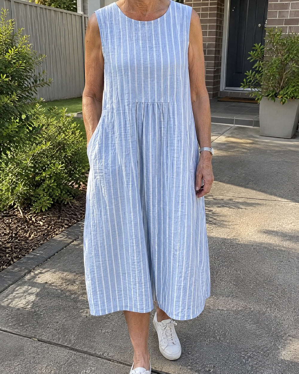 Dina light blue striped sleeveless midi dress worn outside on a garden path