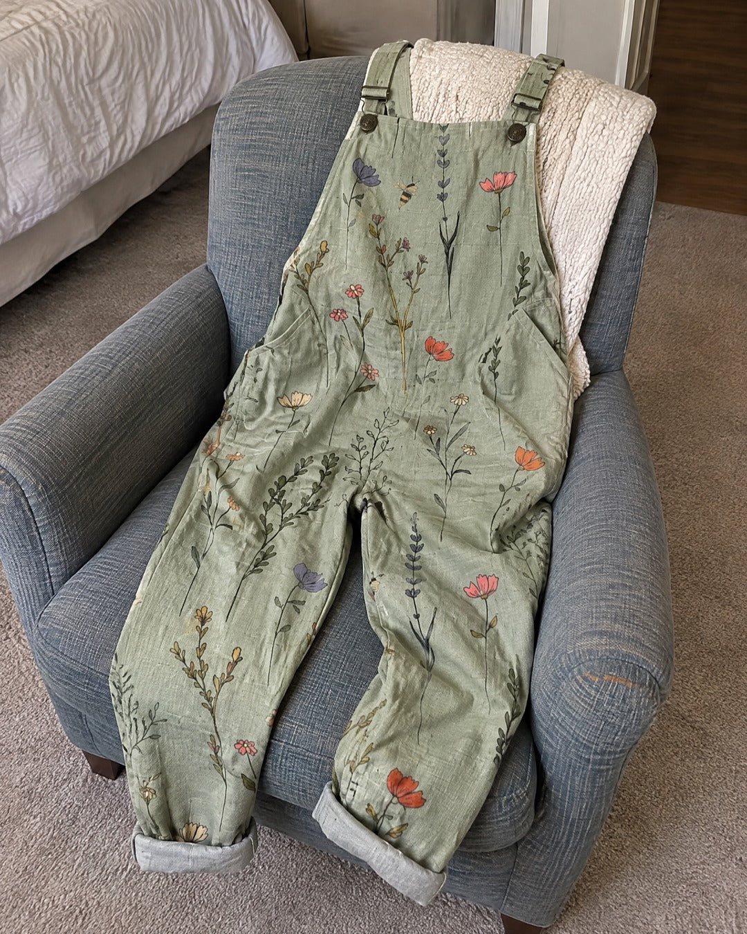 Sage green printed overalls draped on upholstered chair at home showing floral print and rolled hems