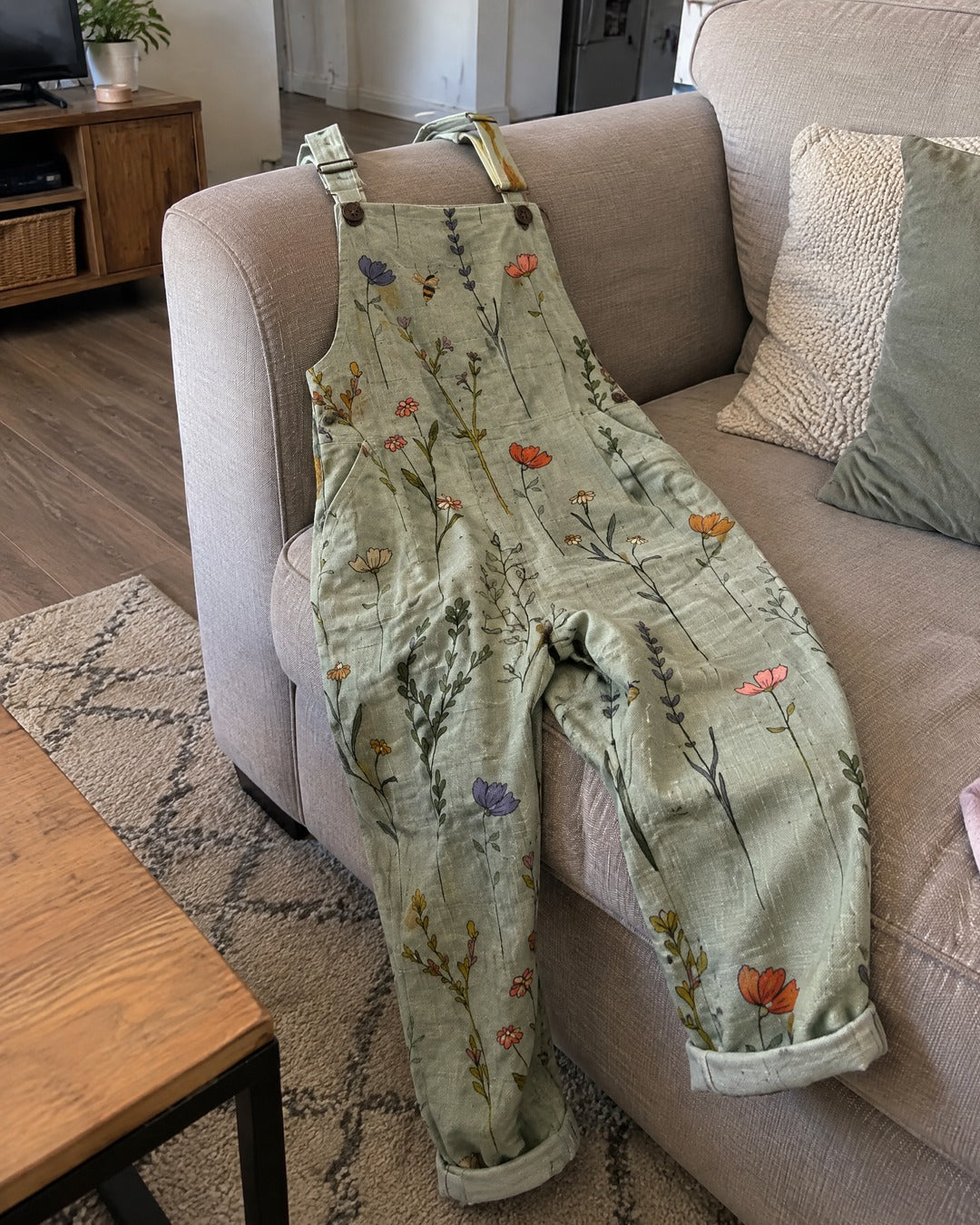 Floral overalls draped over a living room sofa with side pocket and flowers visible
