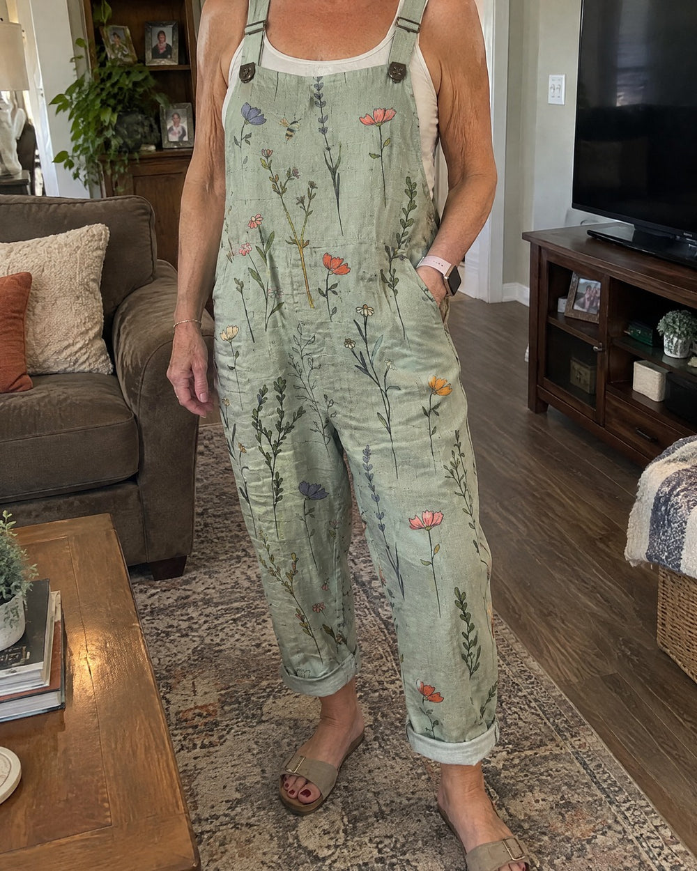 Mature woman wearing sage green printed overalls in living room with hands in pockets