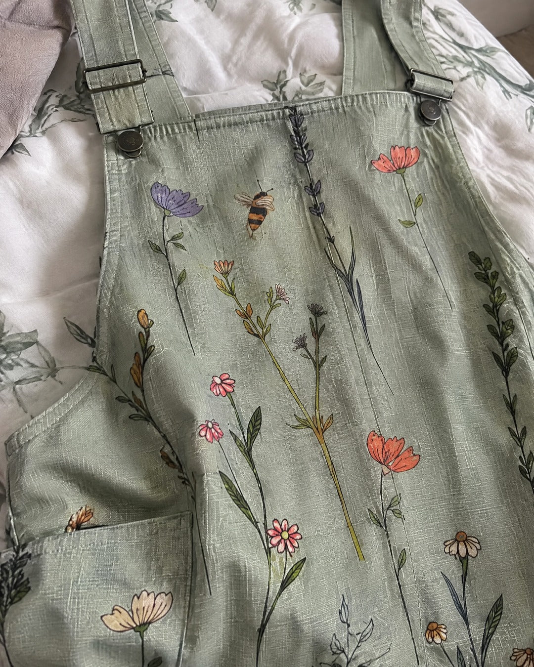 Close-up of green floral overalls showing fabric texture adjustable shoulder straps and small bee print