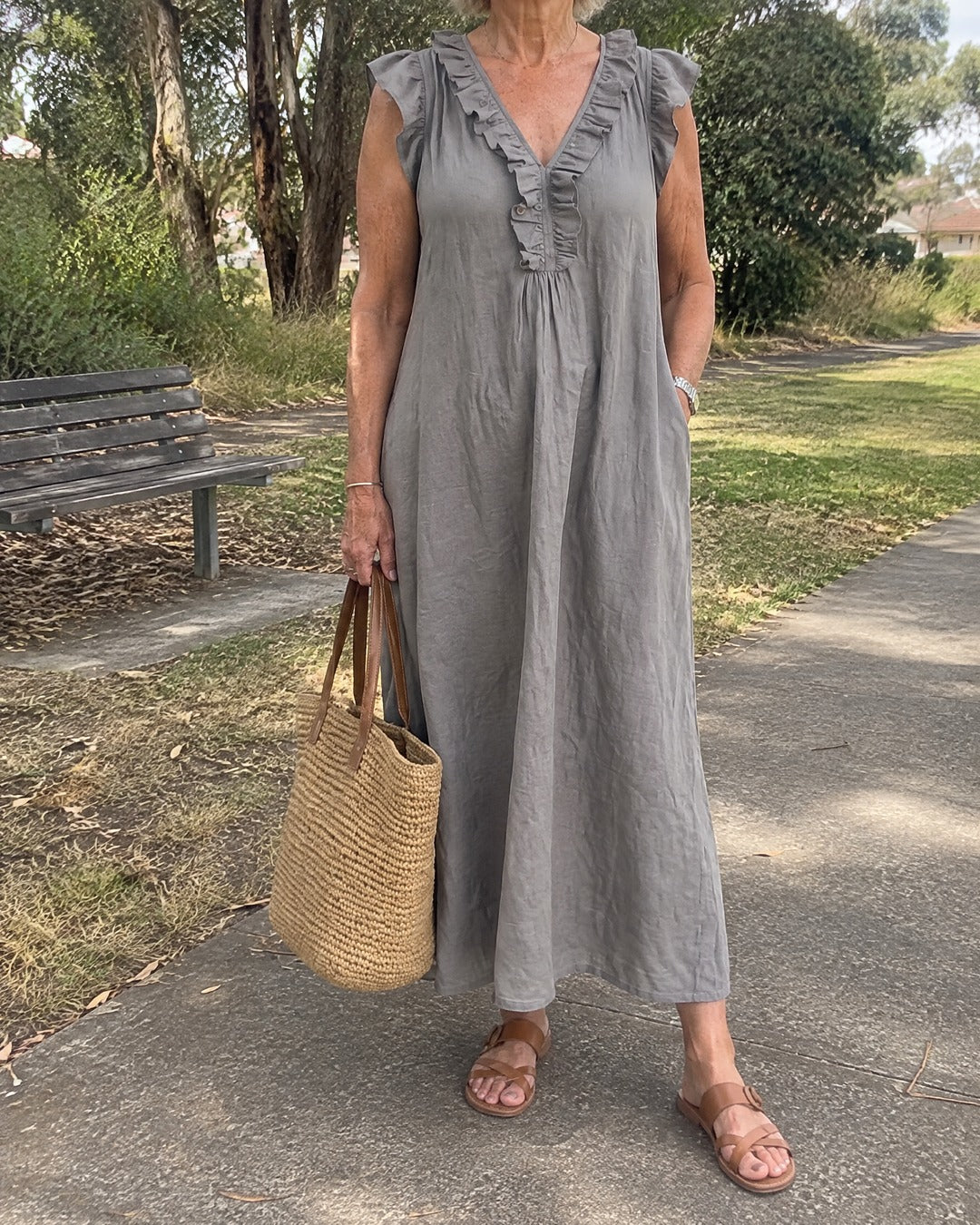 Mature woman outdoors in a grey Josette ruffle V neck maxi dress with a raffia bag