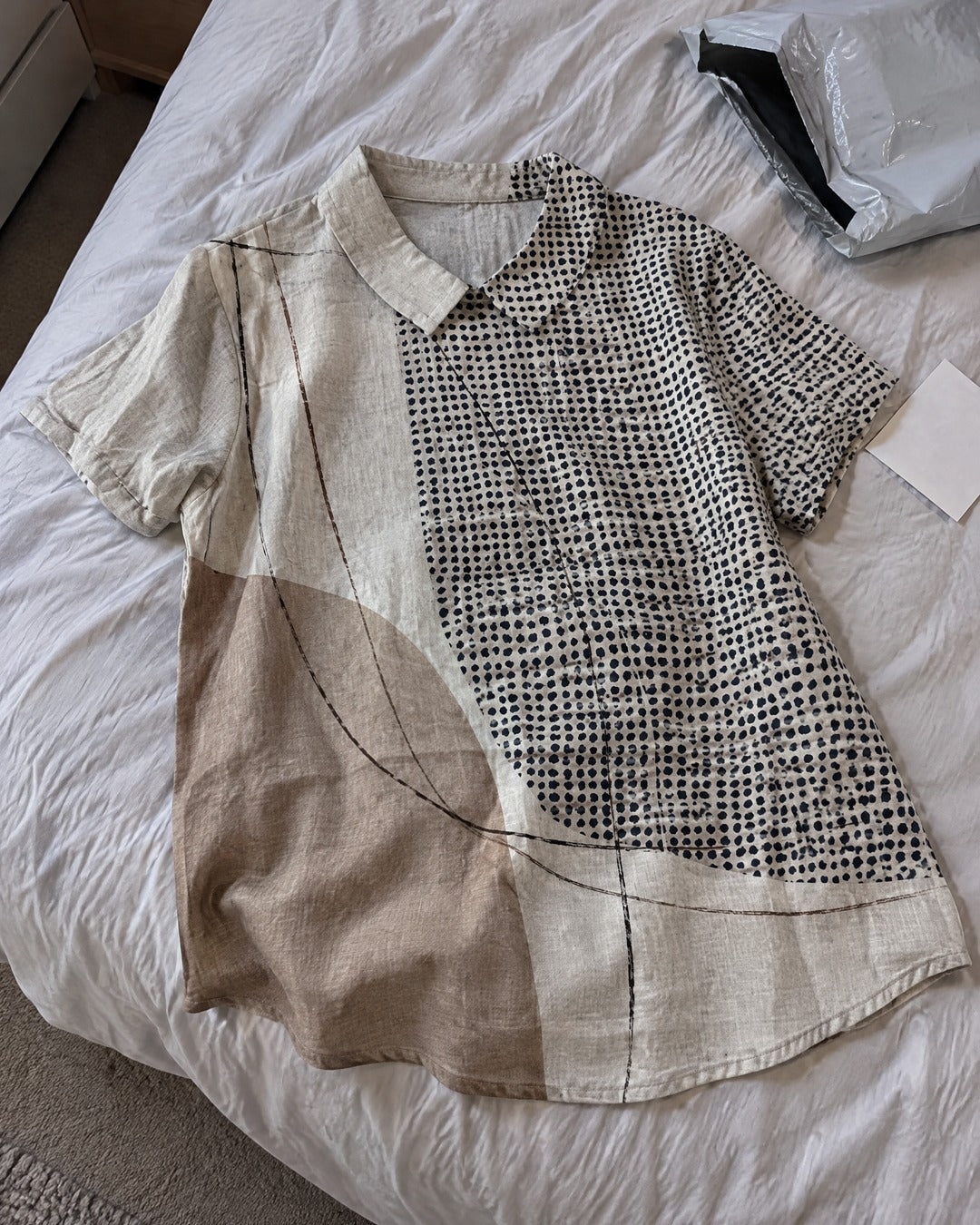 Lana abstract dots and lines short sleeve shirt laid on bed, showing cream, taupe and navy pattern