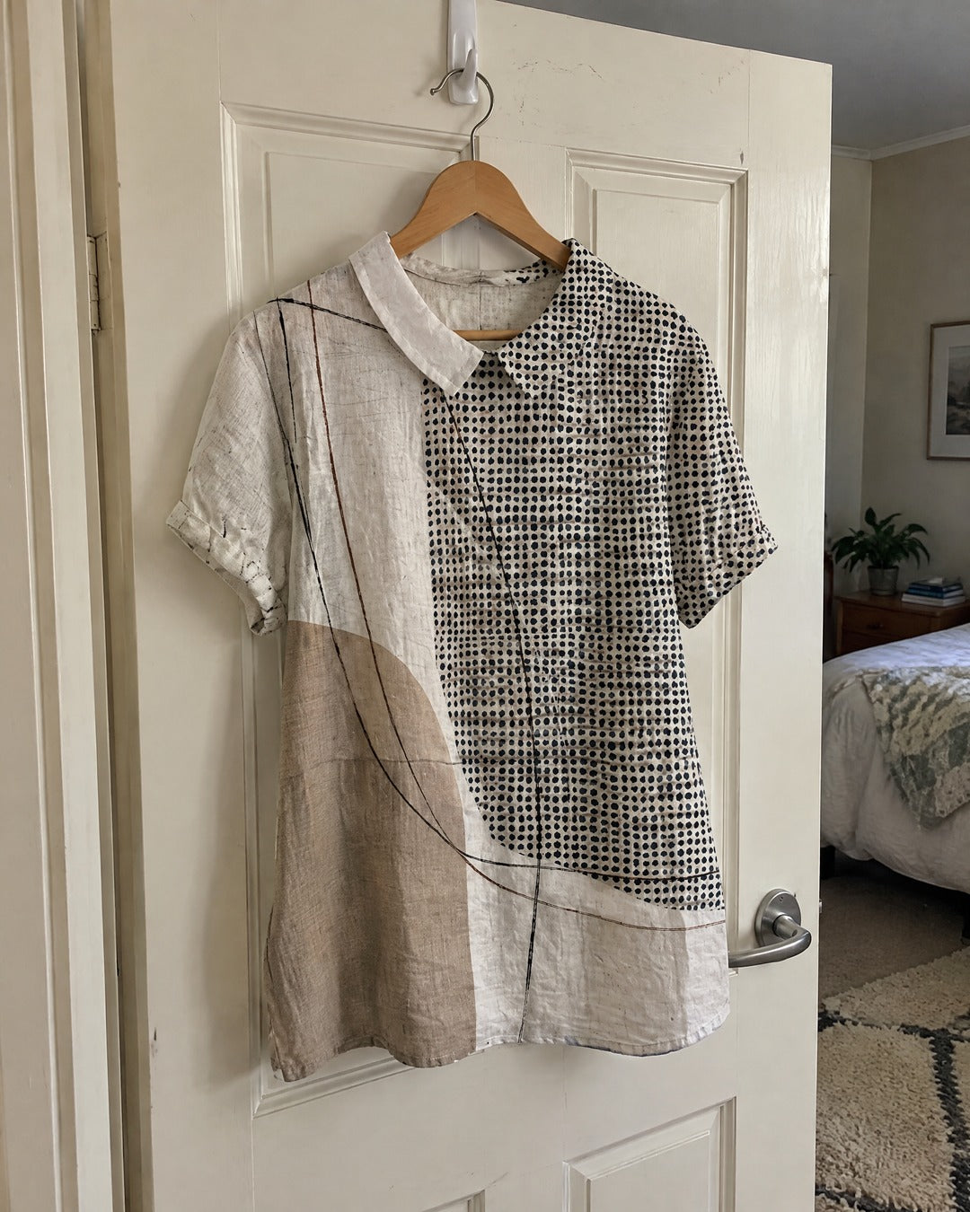 Lana shirt with abstract dots and lines hanging on the back of a bedroom door