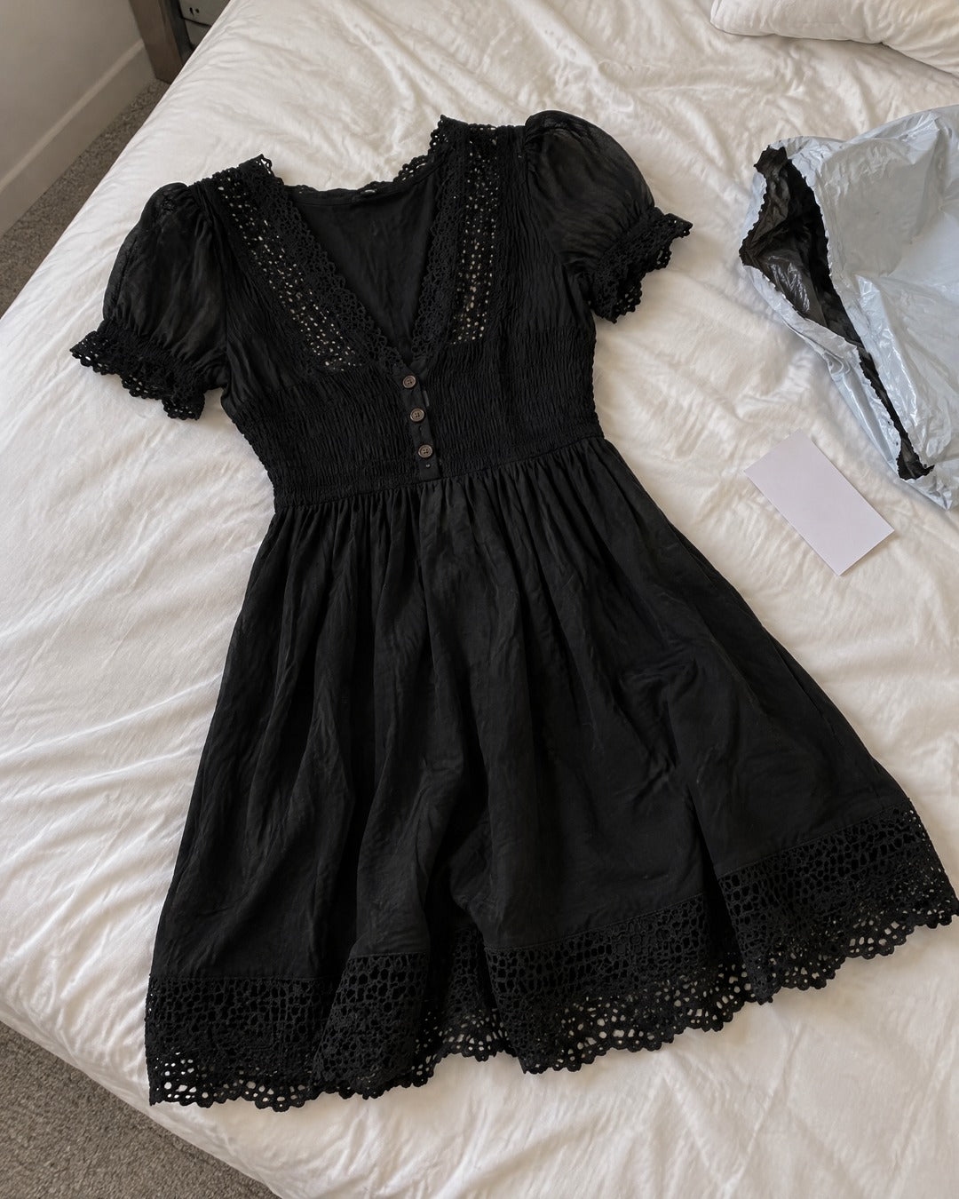 Vivienne black lace-trim smocked dress laid on a bed