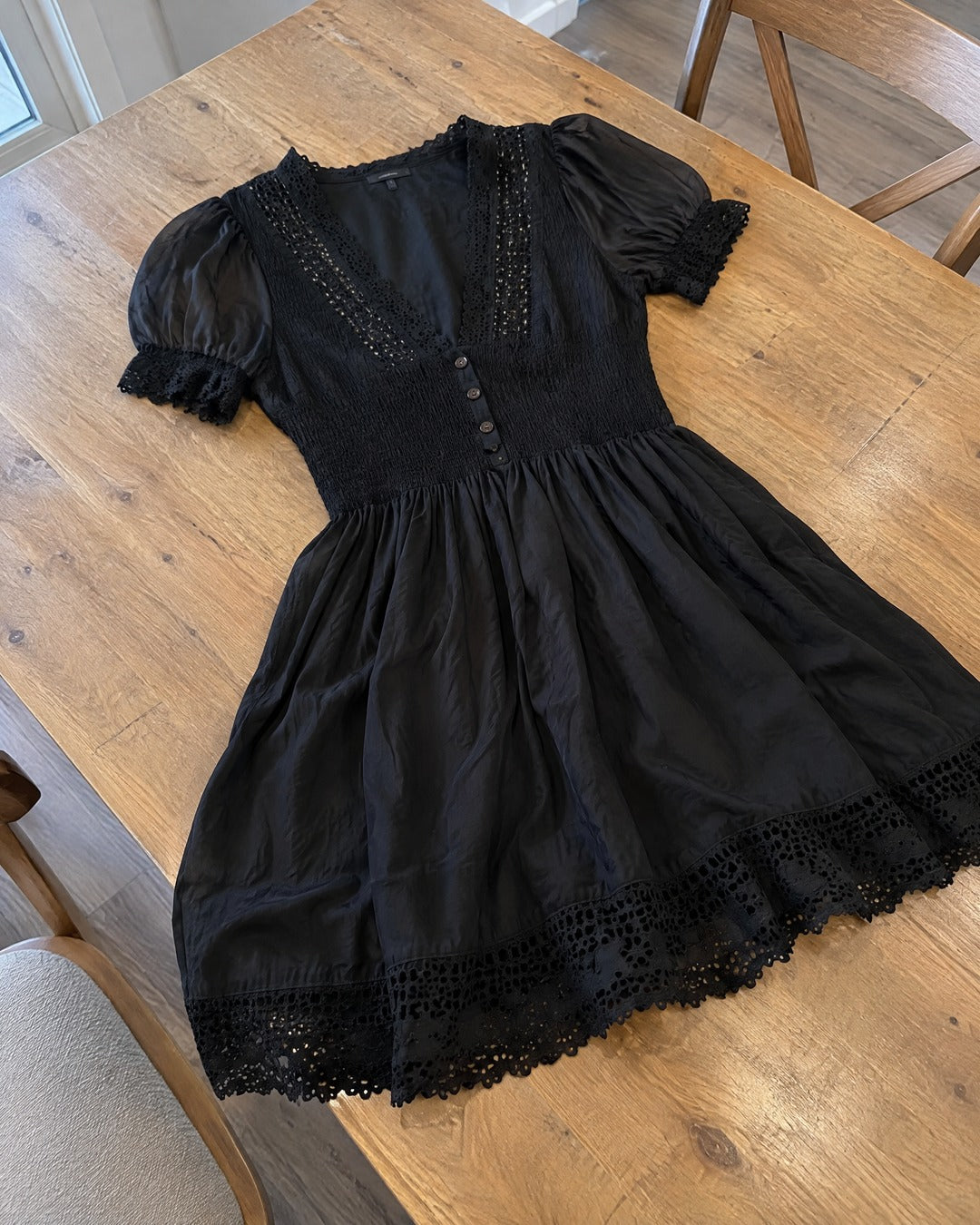 Vivienne black dress spread across wooden dining table, showing lace trim and smocked bodice