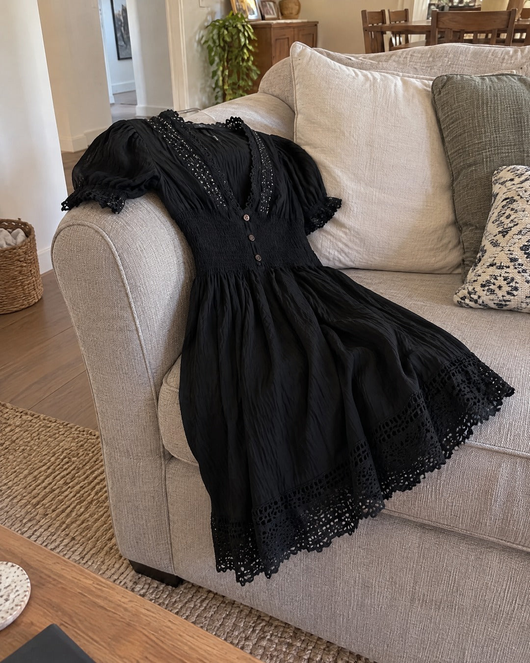Vivienne black dress draped over living room sofa arm, showing lace hem and puff sleeves