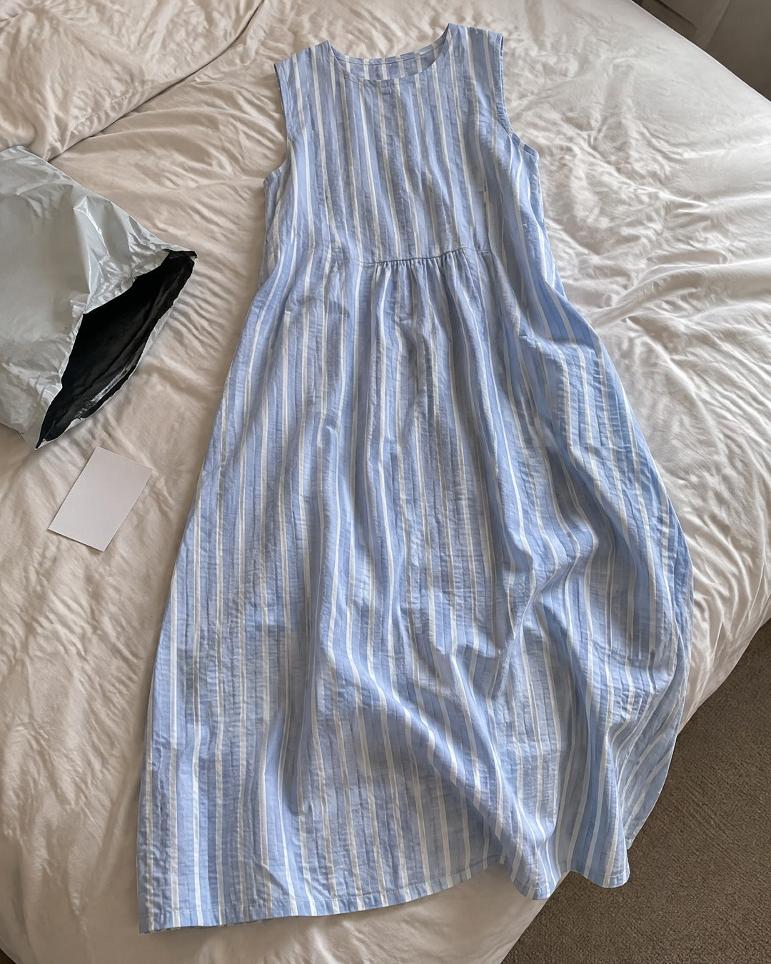 Dina blue striped sleeveless midi dress laid out on a bed